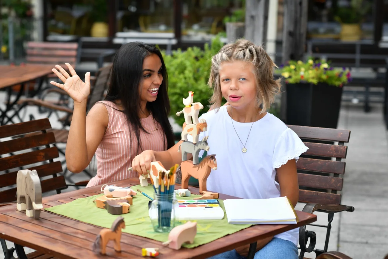Au-pair unterstützt ein Kind geduldig beim Basteln mit Holzfiguren