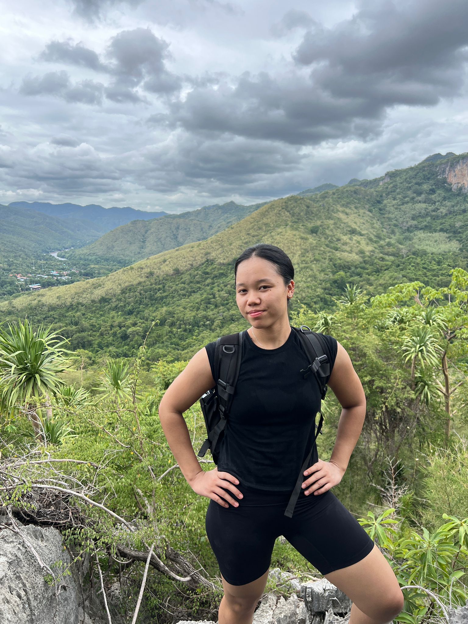 Au-pair Hnin mit Rucksack auf einem Aussichtspunkt vor bewaldeten Bergen.